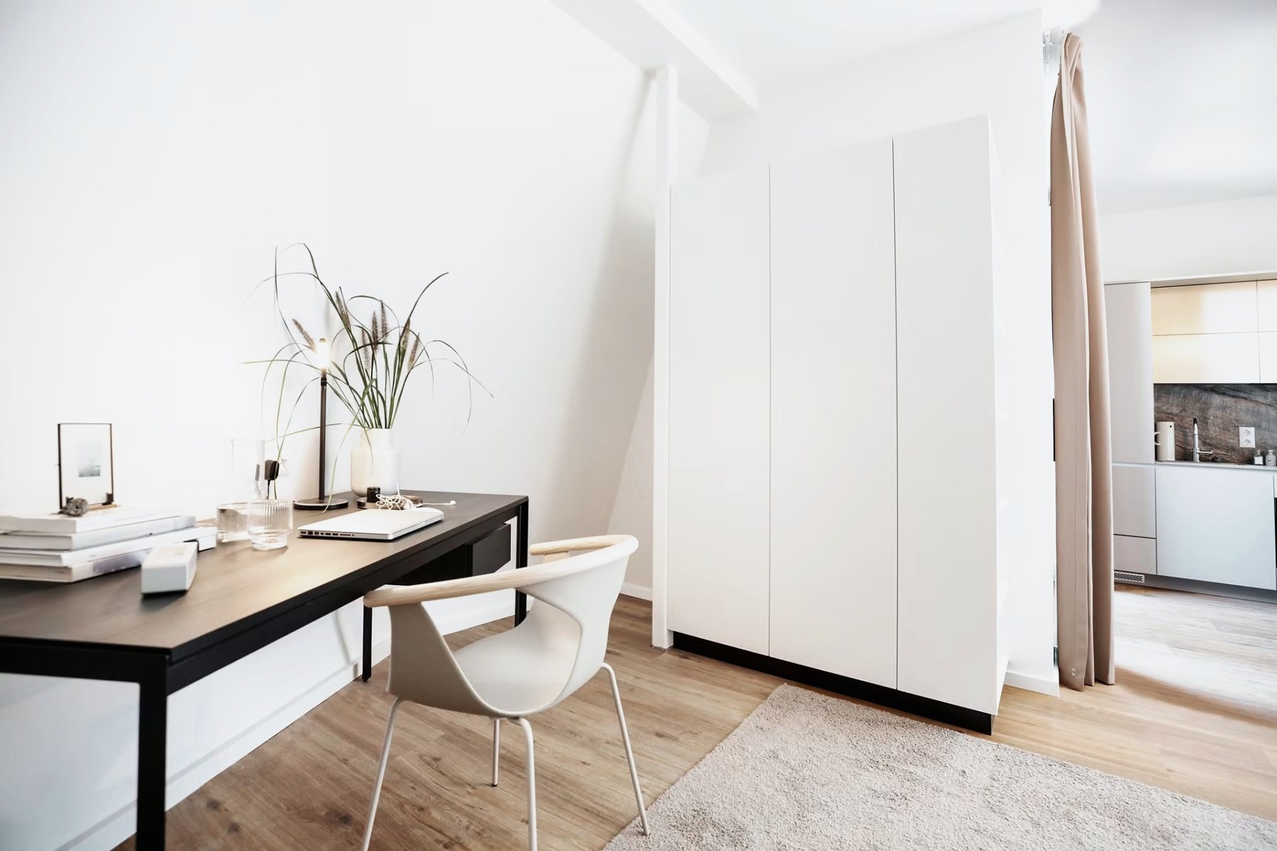 Wohnraum mit Schreibtisch, weißem Schrank und Blick in die Küche